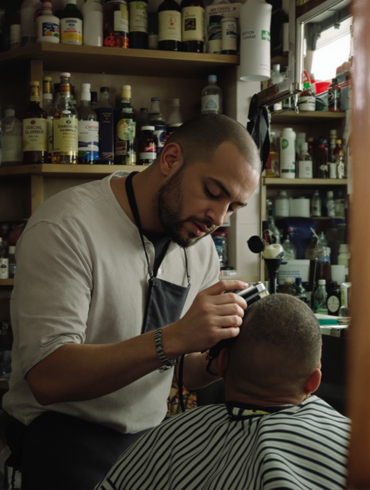 A barber finishing a haircut in his shop, both of them laughing.
